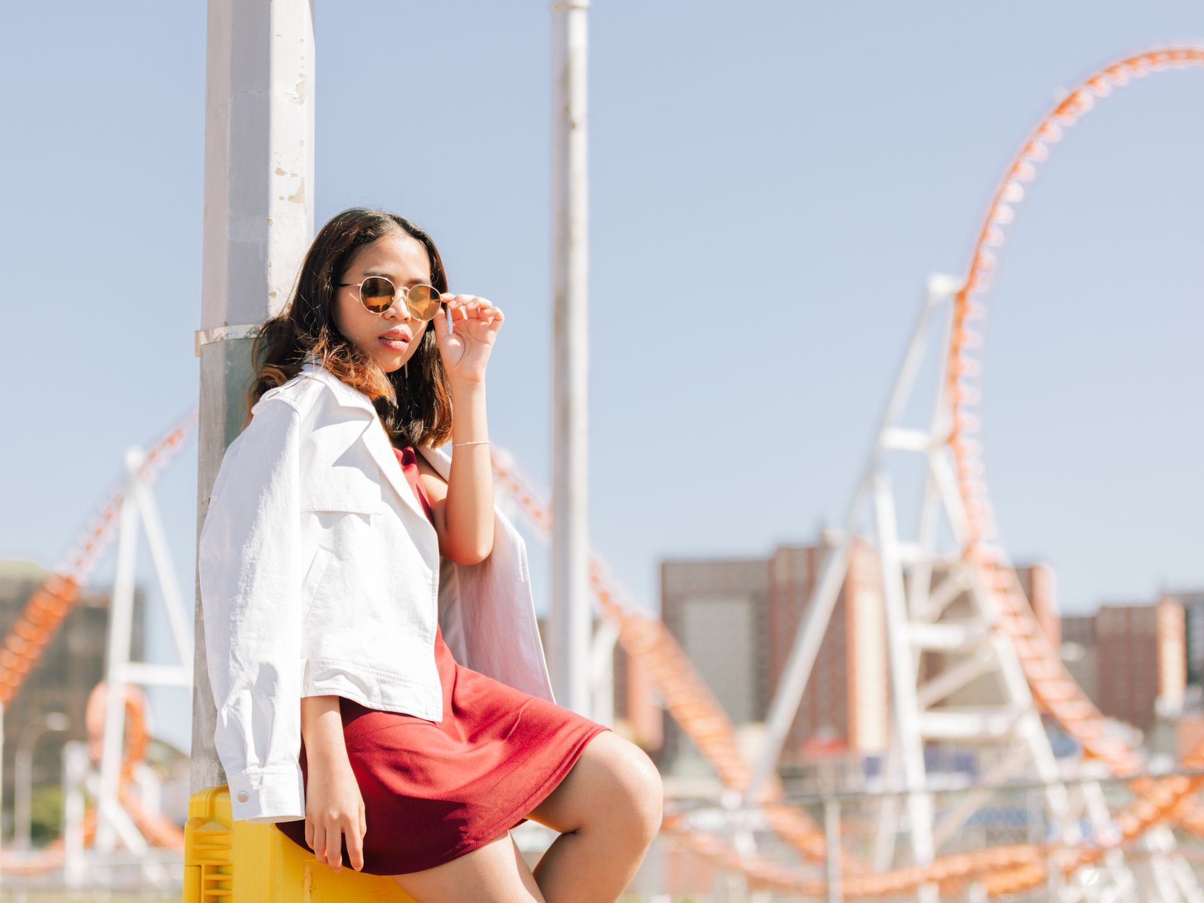 Fashionable woman posing with sunglasses at Coney Island amusement park on a sunny day.