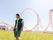 在一个晴天的公园里，便装的人摆着姿势，背景是过山车