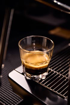 Steaming glass of espresso on a sleek coffee machine in a cozy setting.