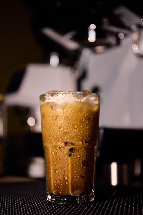 Free Close-up of a cold iced coffee with foam in a cafe setting. Perfectly lit and inviting. Stock Photo
