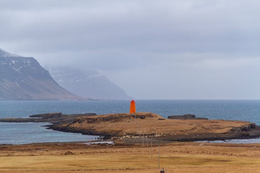 Vibrant orange lighthouse on a remote island with rugged coastal backdrop, capturing nature's raw beauty.