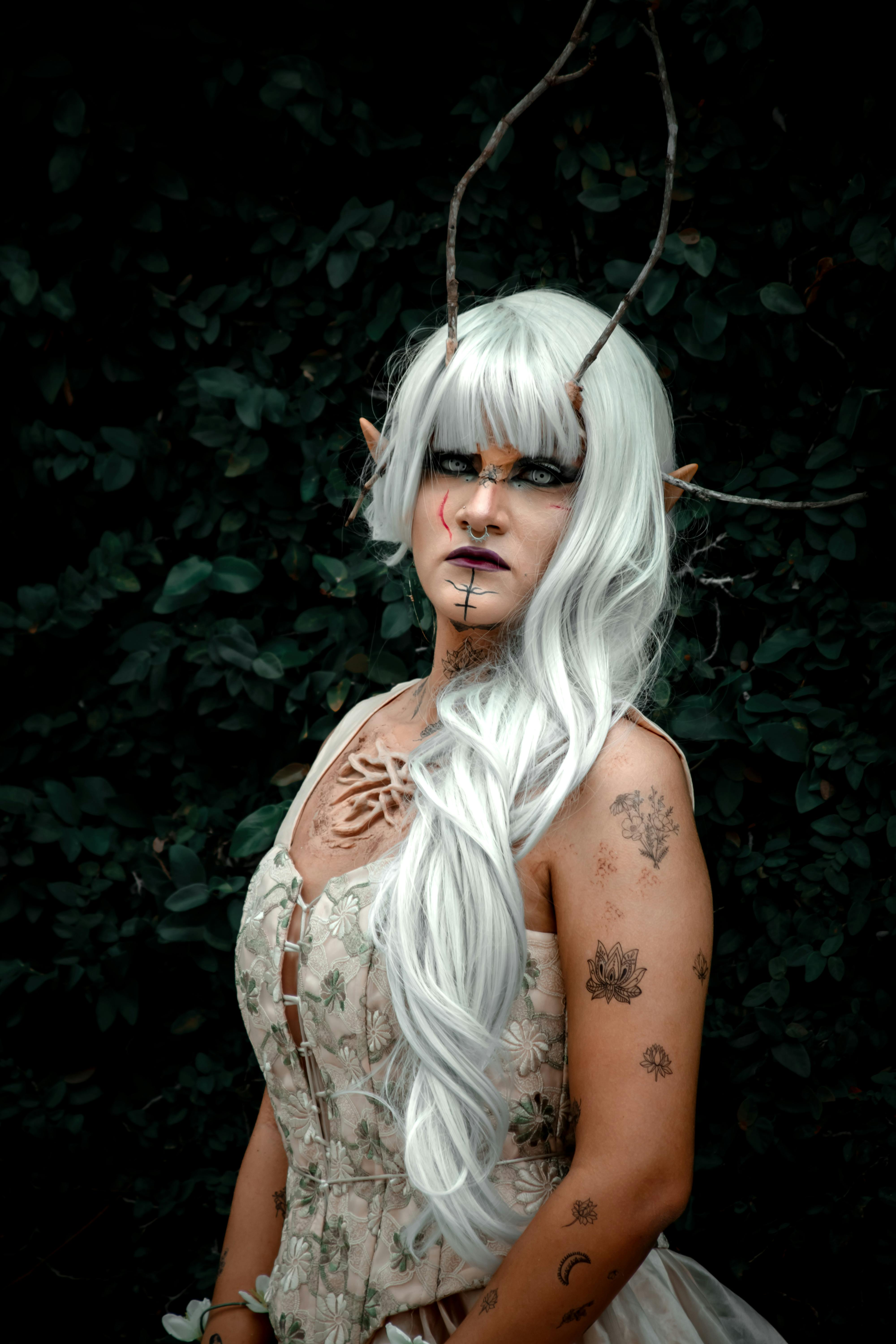 Mystical portrait of a fantasy character with antlers and white hair in a lush forest setting.