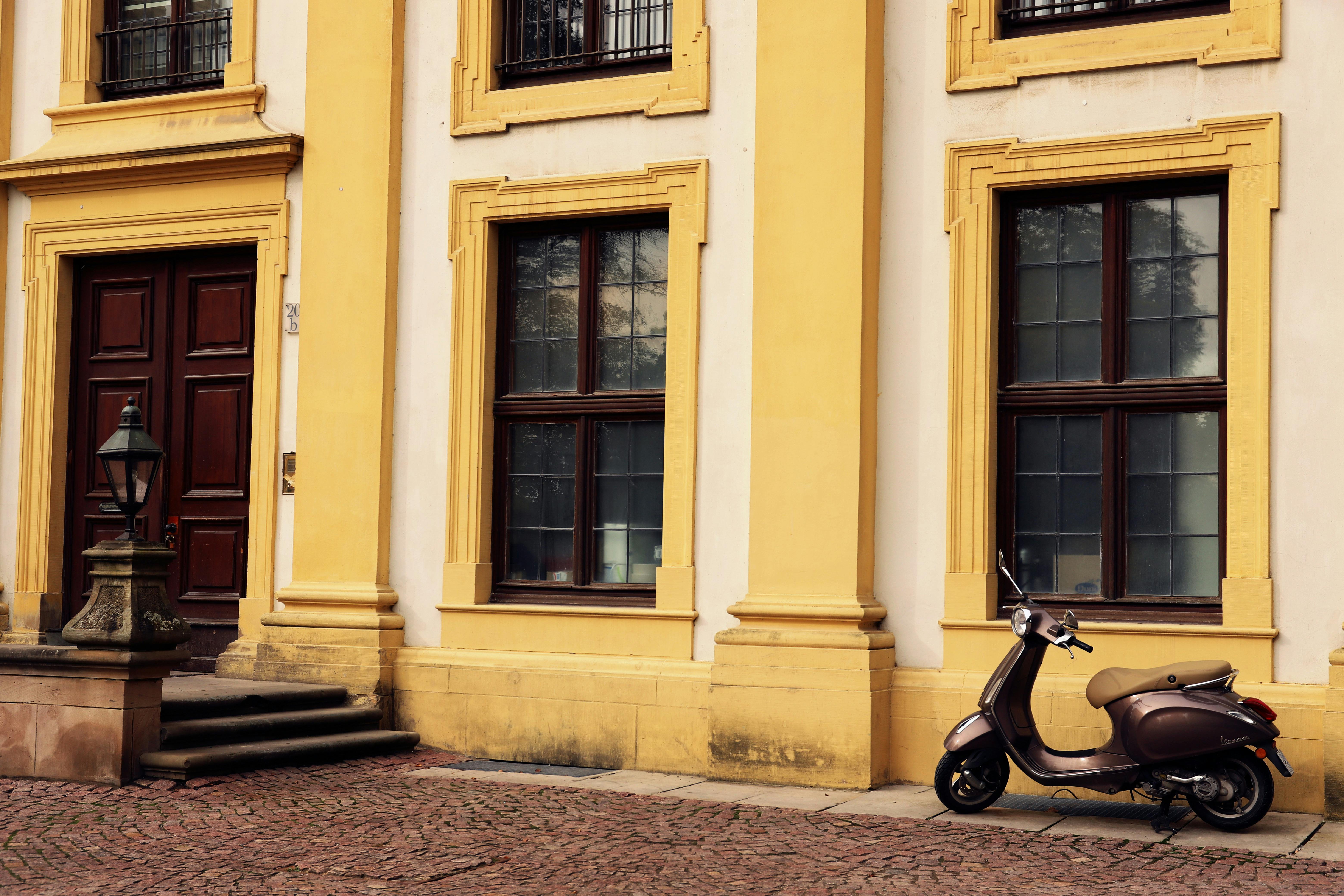 A retro scooter parked by an elegant building facade with ornate details.