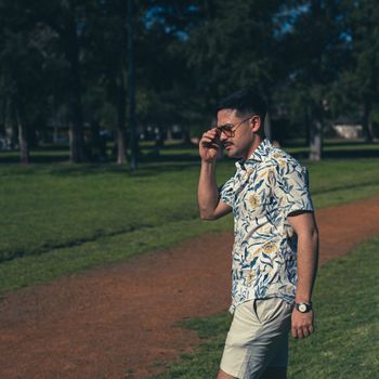 Man in floral shirt walking outdoors in a park.