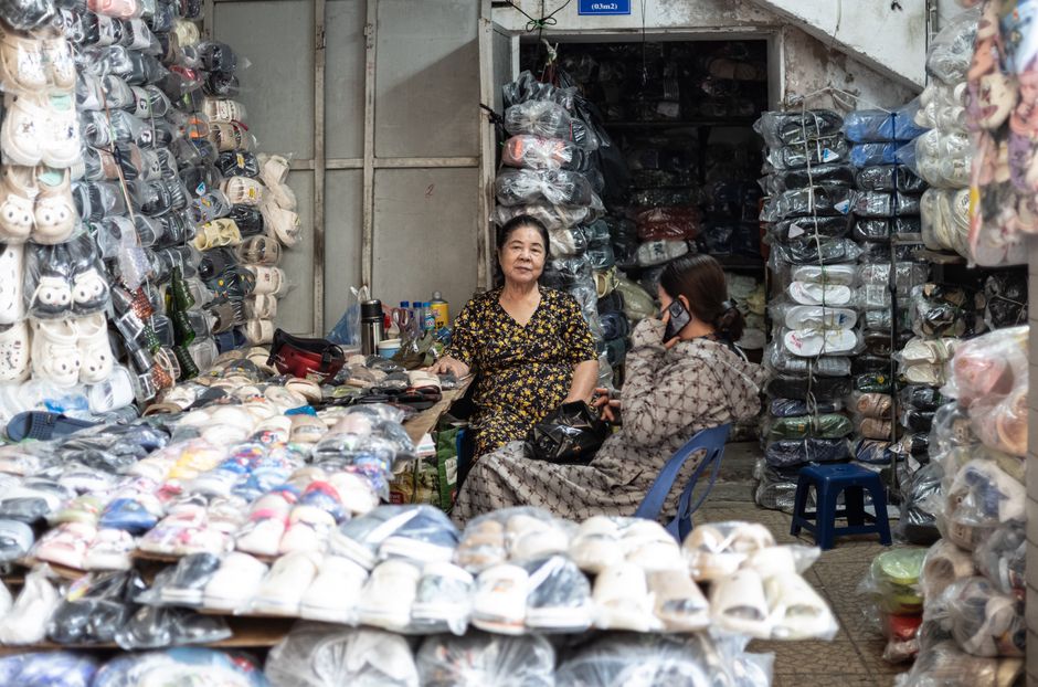 Traditional market in Mong Cai with organized stalls, shoppers bargaining politely, summer clothing and household goods, authentic border trade atmosphere, detailed documentary style