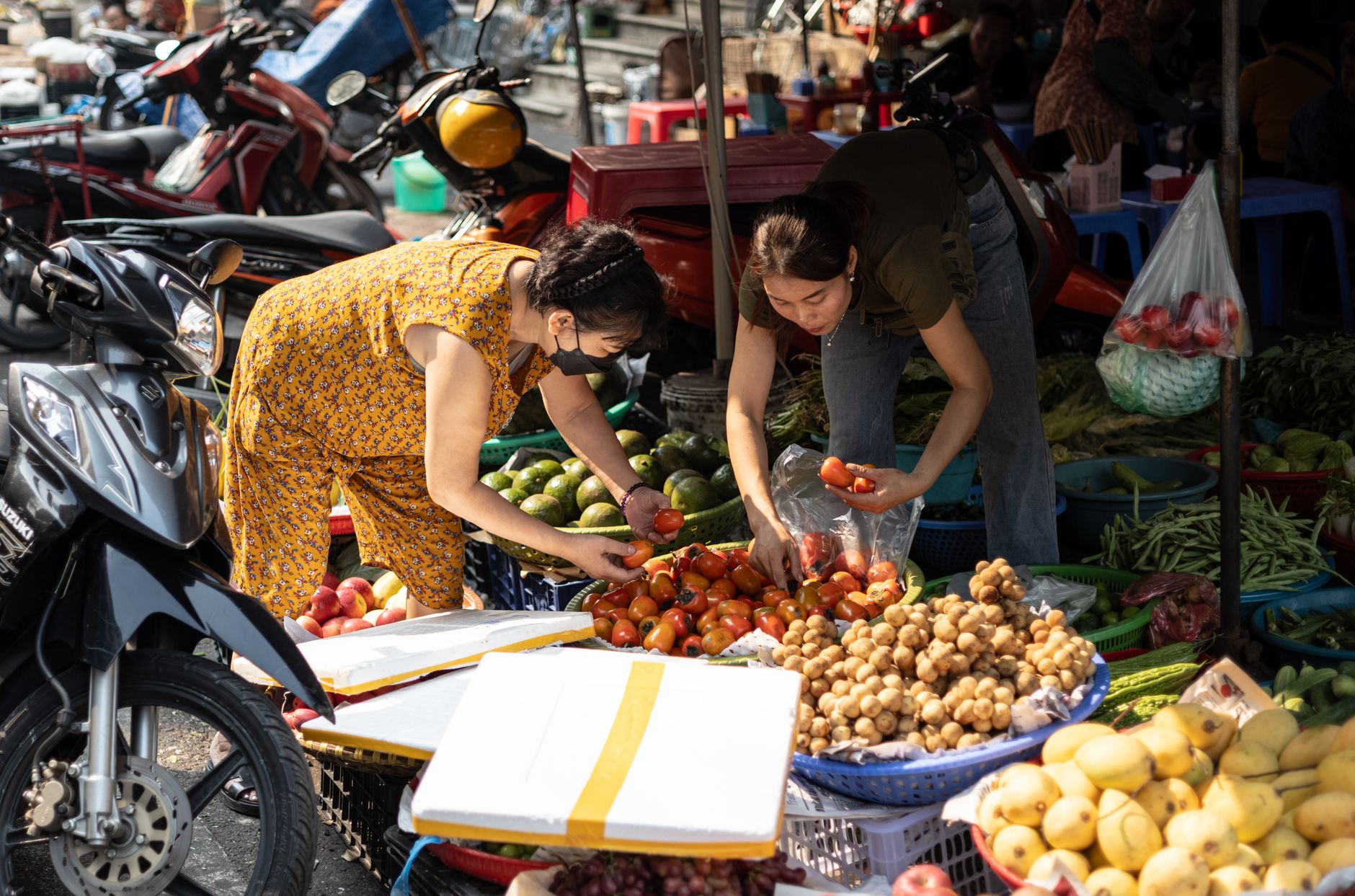 Two women selecting fresh produce at a bustling outdoor market.