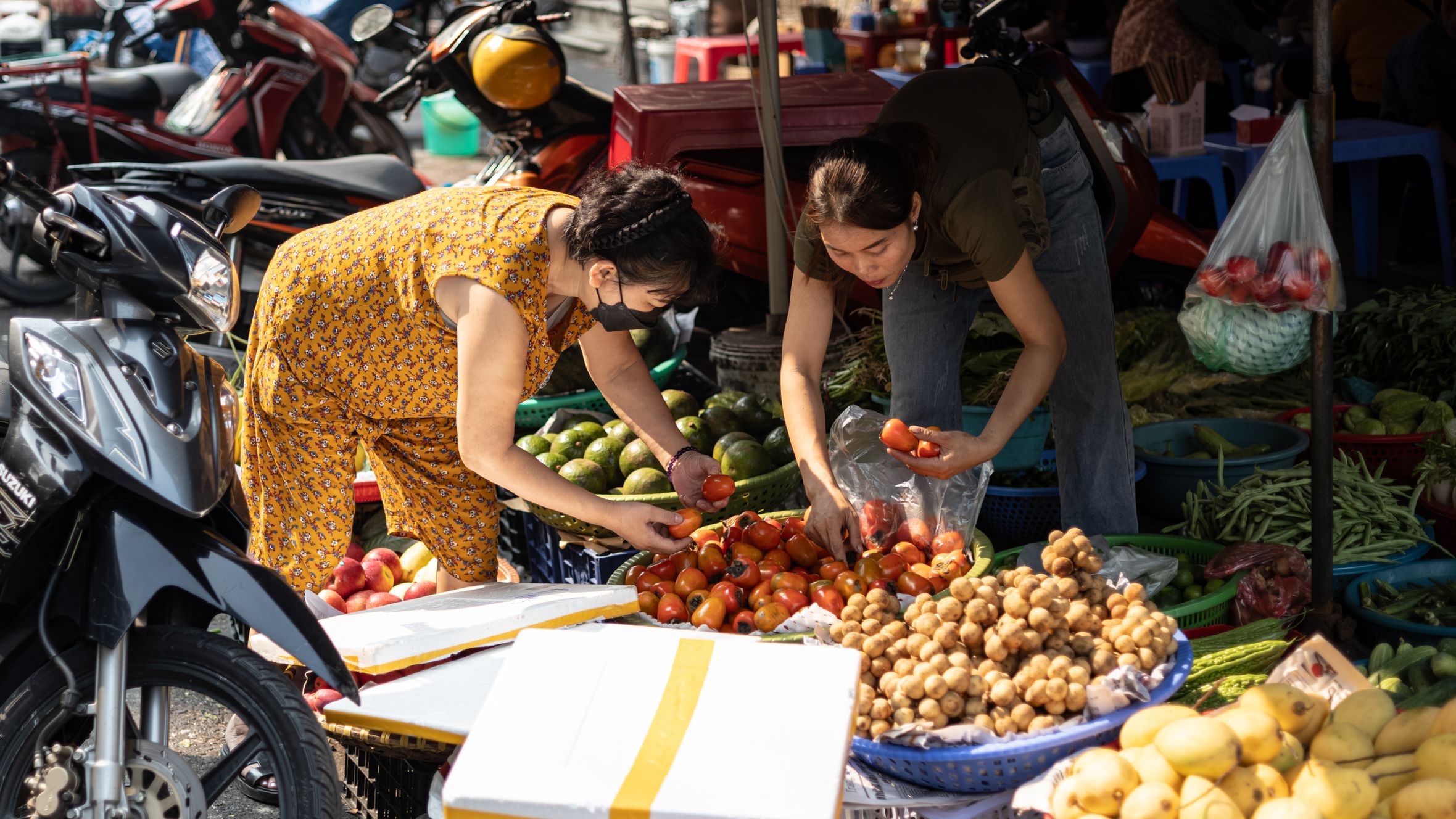 Two women selecting fresh produce at a bustling outdoor market.