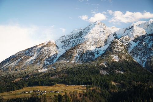 Free Majestic snowy mountain range with pine forest and village below, captured on a clear day. Stock Photo