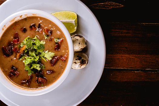 A savory bean soup garnished with herbs, quail eggs, and lime, perfect for a hearty meal.