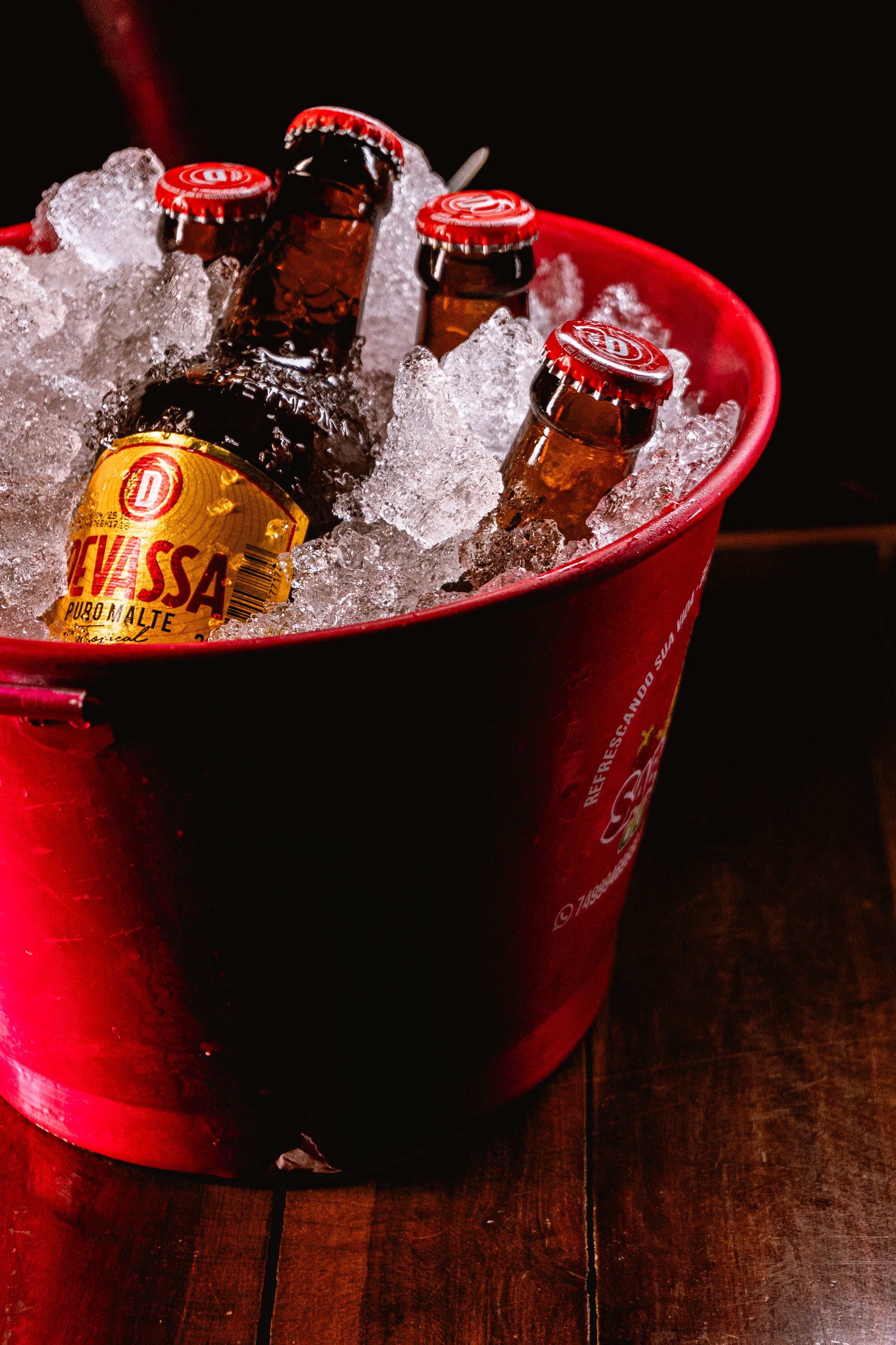 Chilled beers in a red bucket filled with ice on a wooden table, perfect for a refreshing drink.