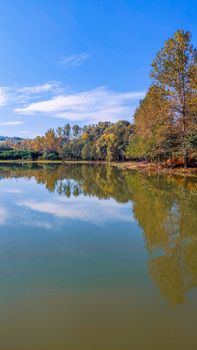 Tranquil lake scene with autumn trees reflecting in still water under a clear blue sky.
