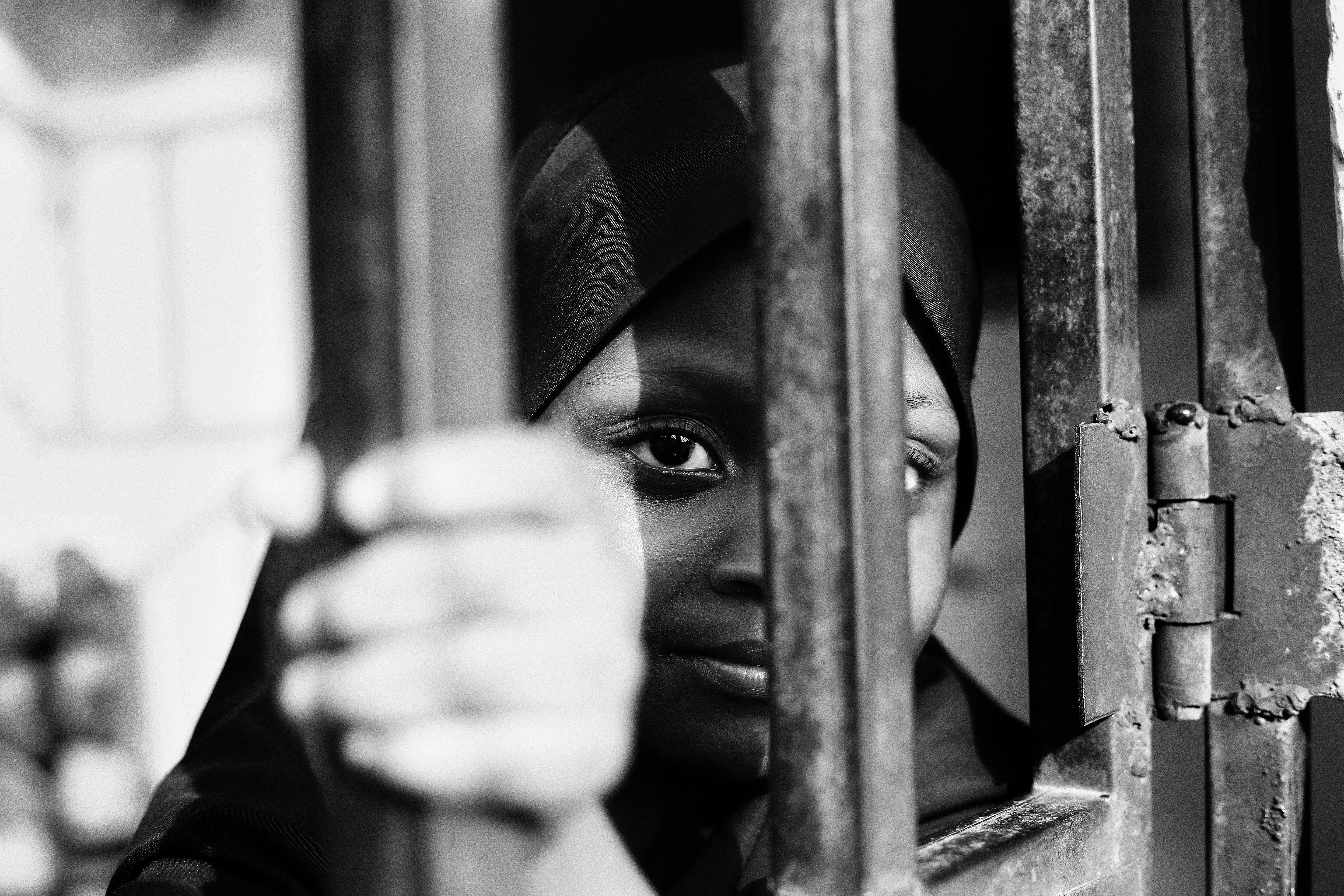 Black and white portrait of a child peering through bars in Abuja, Nigeria.