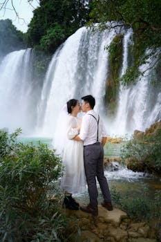 A couple embraces by the majestic Ban Gioc Waterfall, capturing a romantic moment in nature.