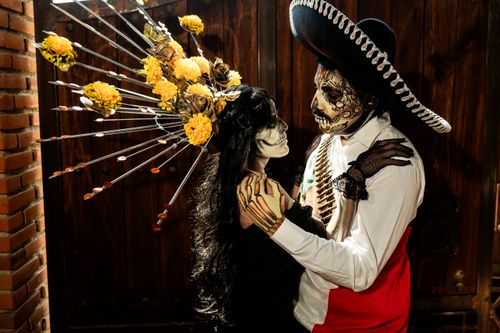 Free A couple dressed in Día de los Muertos costumes with intricate face paint embrace indoors. Stock Photo
