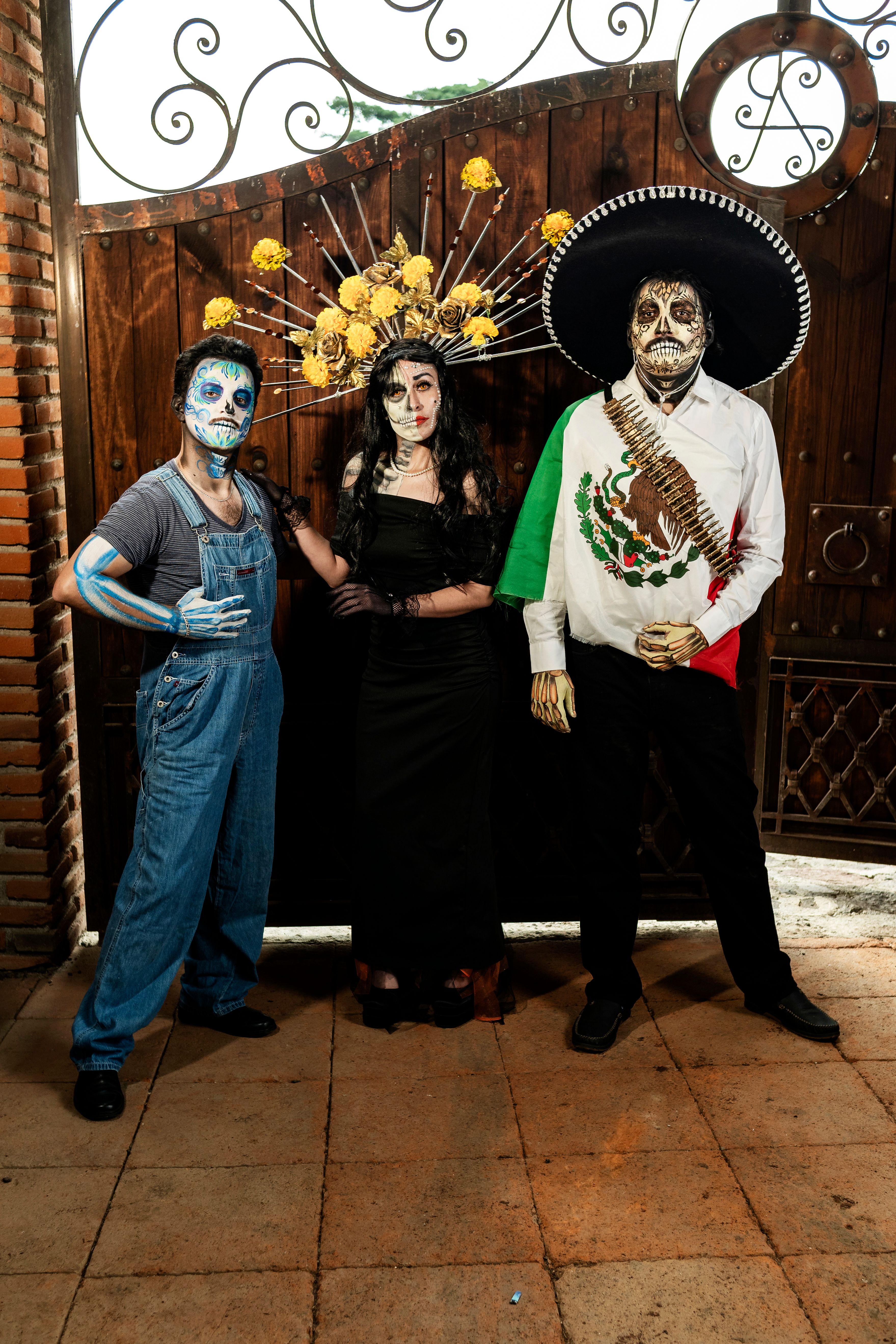Three people dressed in traditional Day of the Dead costumes posing with striking face paint and accessories.