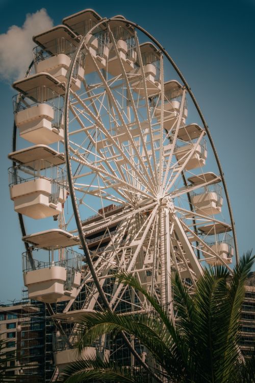 Free A towering Ferris wheel stands against a clear blue sky with urban buildings in the background. Stock Photo