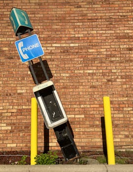 A broken vintage payphone leaning against a brick wall, symbolizing communication history.