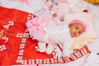 Cute baby in pink outfit on vibrant African textile with shells.