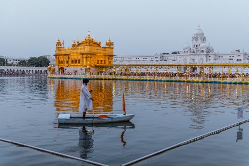 Free A Sikh man paddles a boat near the illuminated Golden Temple in Amritsar at dusk. Stock Photo