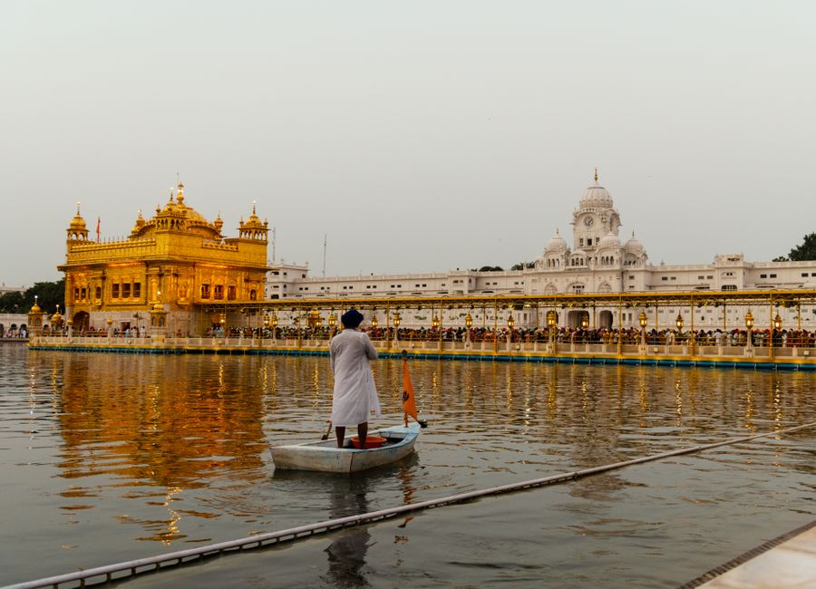 A Sikh man paddles a boat in front of the iconic Golden Temple in Amritsar at sunset.