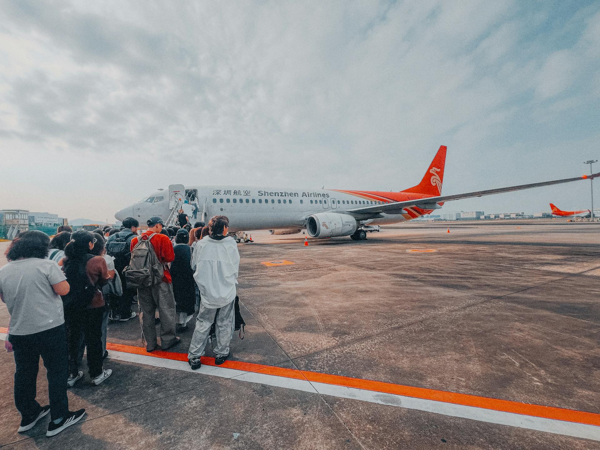 Passengers line up to board a Shenzhen Airlines aircraft on a cloudy day. Travel and adventure await.