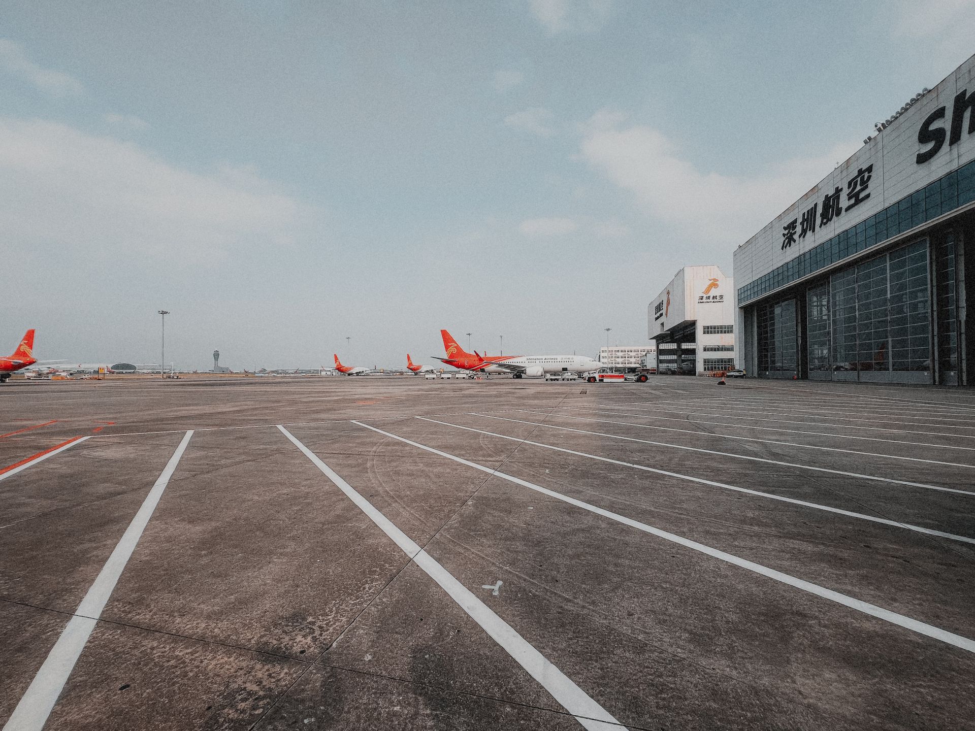 A spacious airport runway featuring airplanes and hangars under a clear sky.