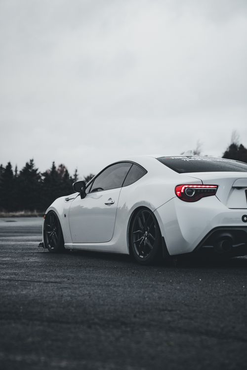 Free A modern white sports car parked outdoors on a cloudy day with trees in the background. Stock Photo