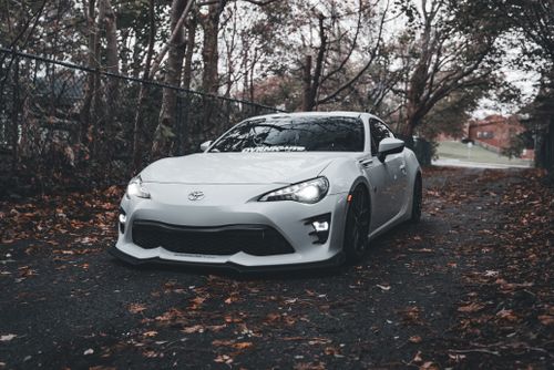 Free White sports car on a leafy outdoor road, capturing autumn vibes. Stock Photo