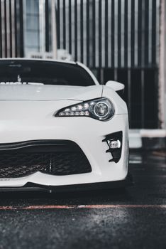 Close-up of a sleek white sports car's front view against an urban backdrop, showcasing modern design.