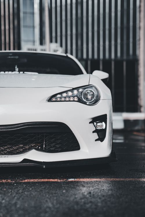 Free Close-up of a sleek white sports car's front view against an urban backdrop, showcasing modern design. Stock Photo