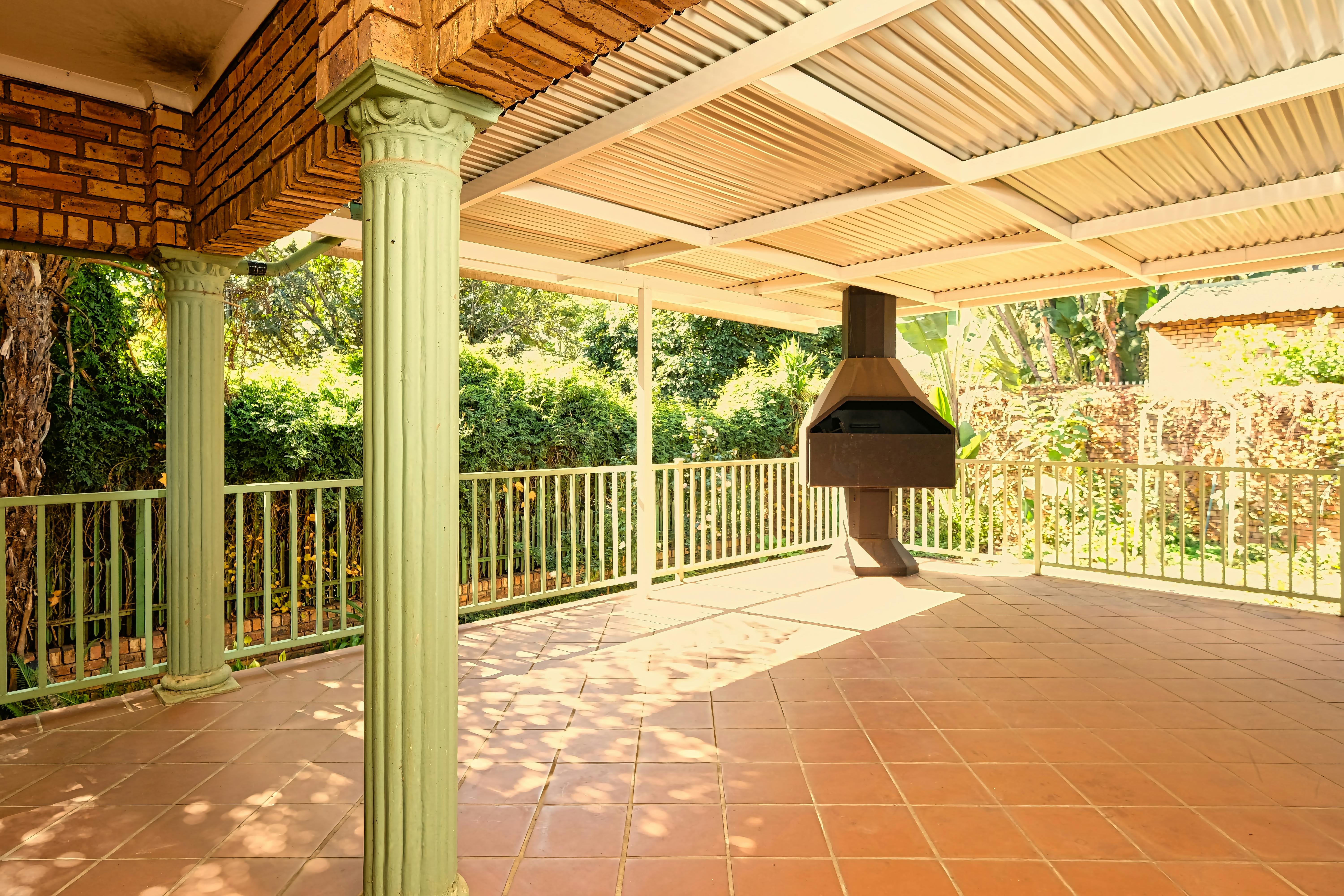 Sunlit outdoor patio featuring brick pillars, iron railings, and a built-in barbecue.