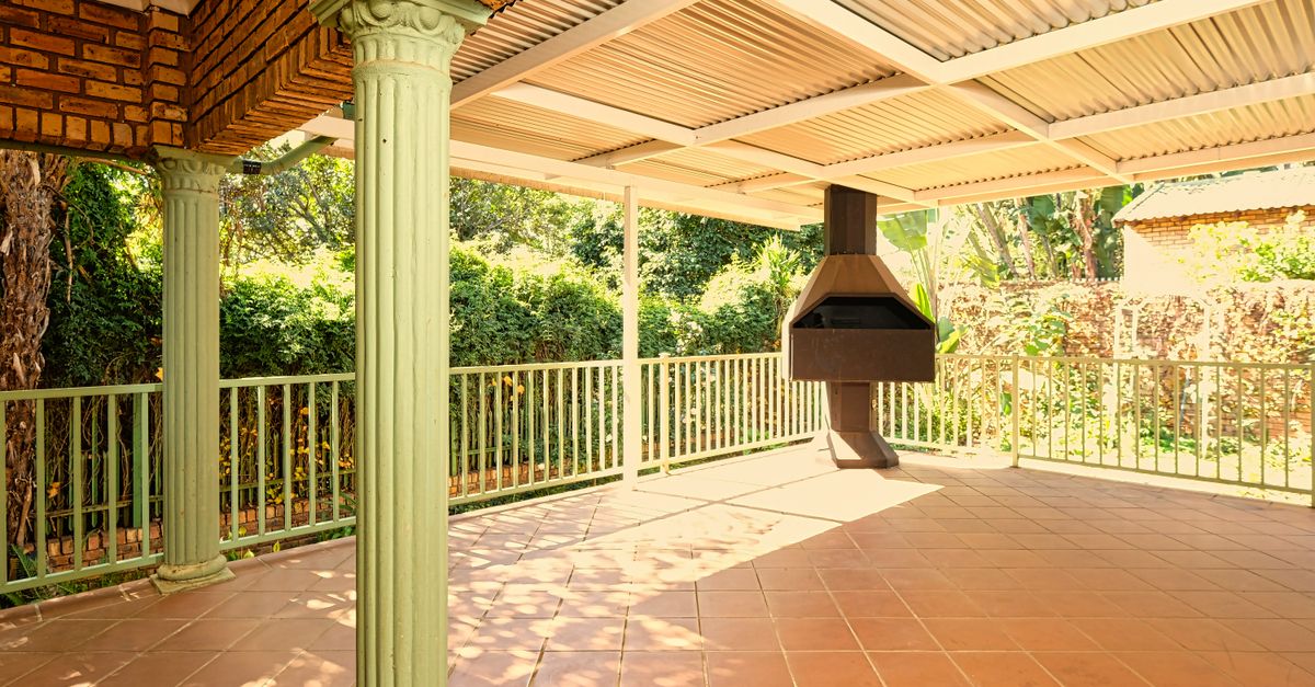 Sunlit outdoor patio featuring brick pillars, iron railings, and a built-in barbecue.