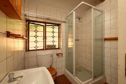 Compact bathroom with tiled walls, glass shower, and natural lighting from a decorative window.