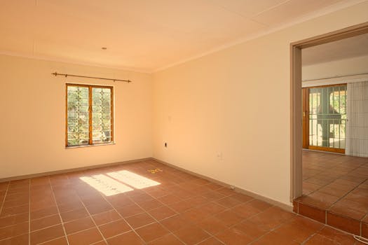 Bright and empty sunlit room with terracotta tiles and wooden window frame interior.