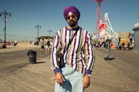 阳光明媚的日子里，一位戴着太阳镜和头巾的时尚男子在科尼岛木板路上摆着姿势