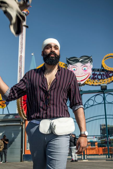 Bearded man in turban posing fashionably at Coney Island amusement park on a sunny day.