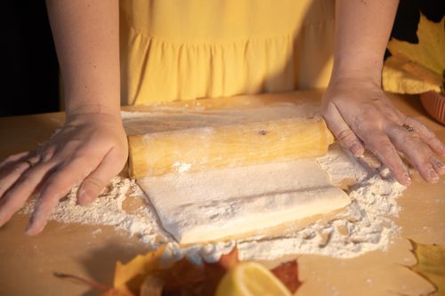 Free Hands rolling dough on a floured surface with fall leaves nearby. Stock Photo
