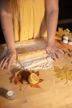 Hands preparing dough with autumn leaves and lemon in kitchen.