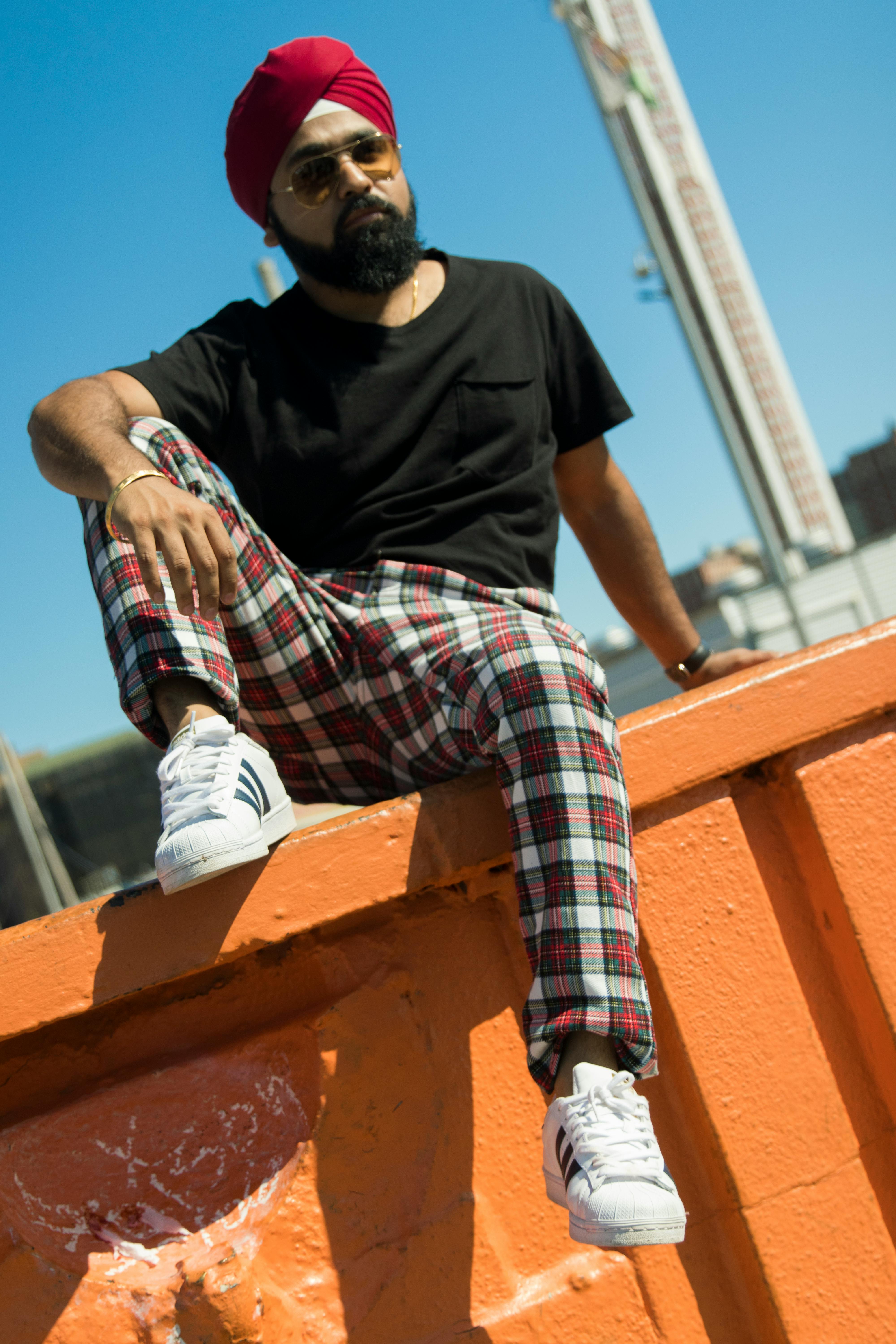 一名穿着格子裤的男子坐在橙色建筑上，进行阳光明媚的时尚拍摄