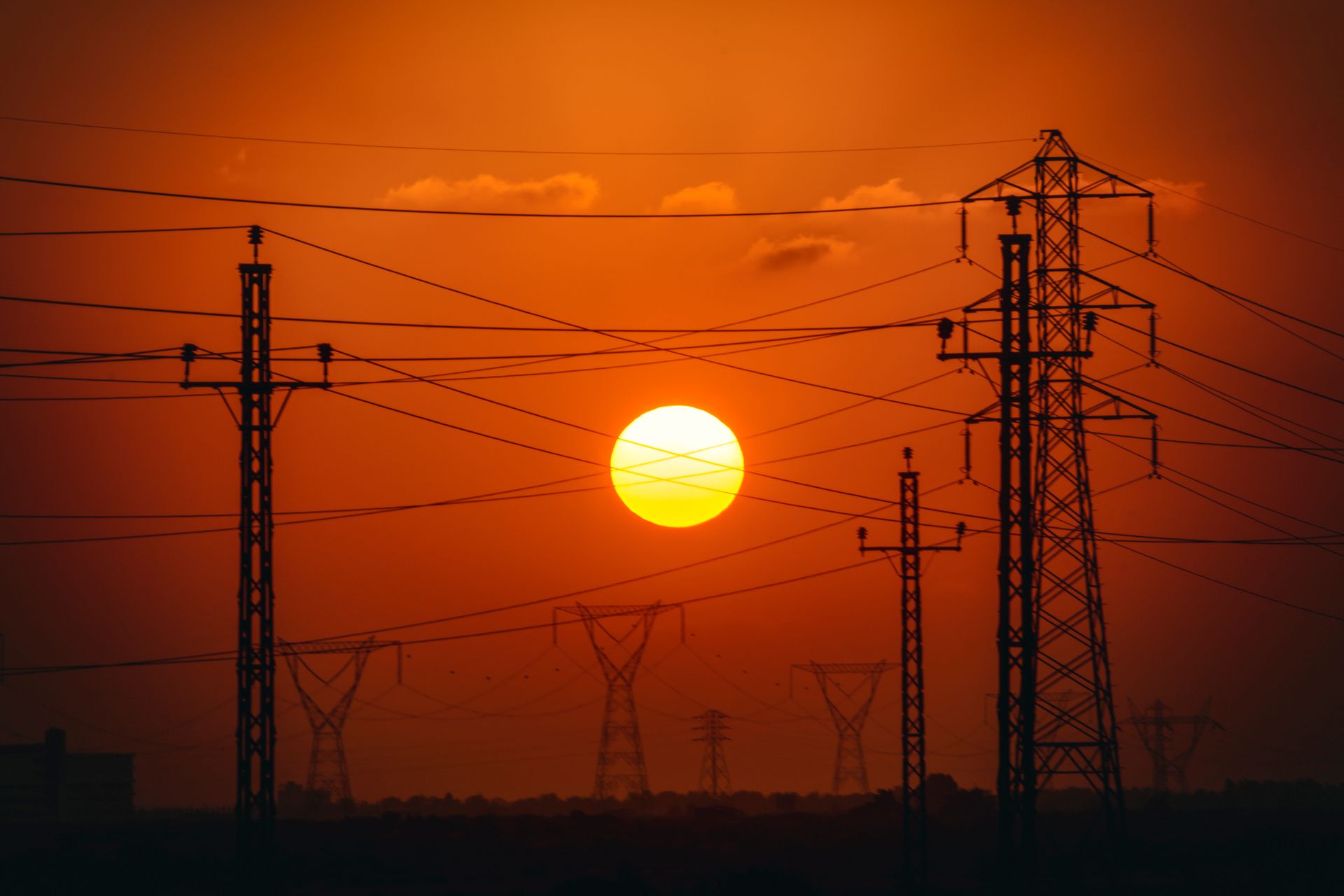 Silhouetted power lines against a vivid orange sunset in Egypt.
