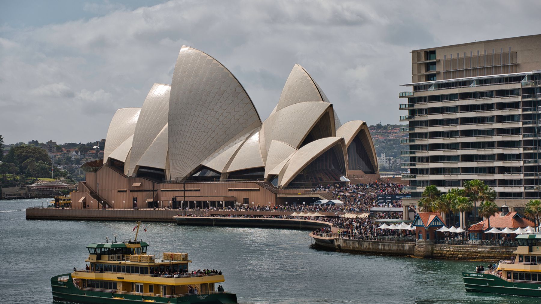 Sydney Opera House waterfront alive with visitors and a passing harbour ferry