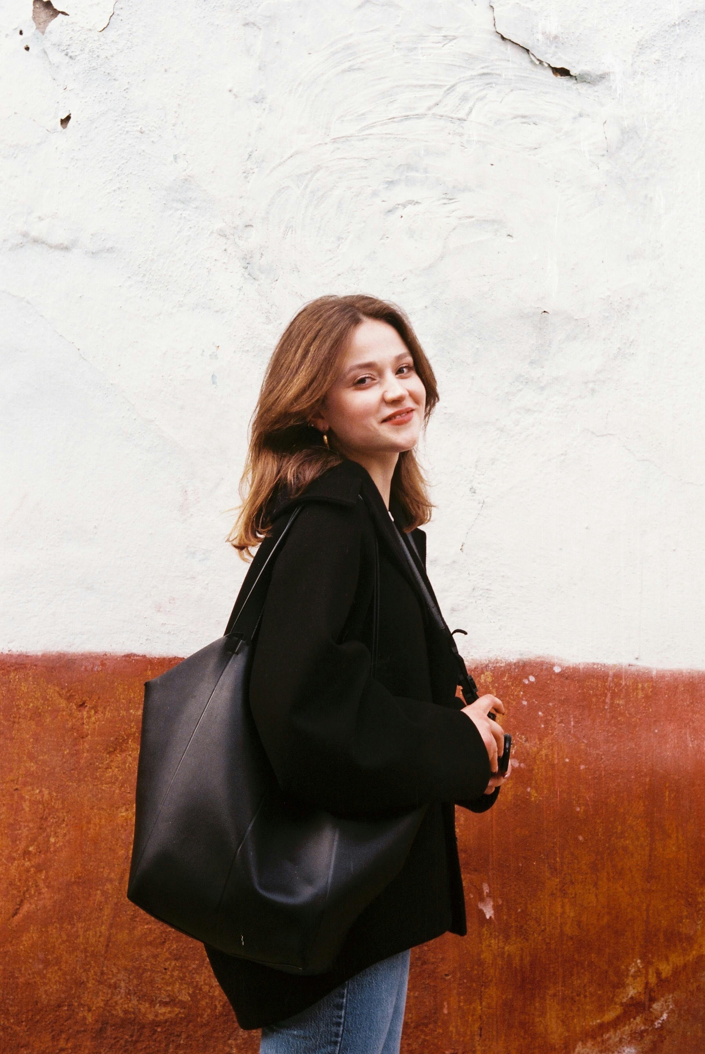 Smiling young woman in casual attire walking with a black bag in Bursa, Türkiye.