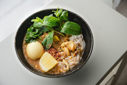 Delicious Burmese noodle soup with egg, spices, and fresh mint garnished in a black bowl.