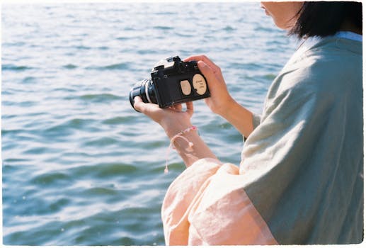 Person holding vintage camera by a serene waterfront. Summer vibes.