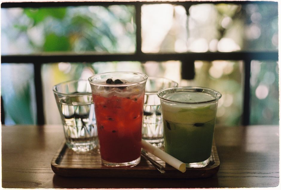 Two refreshing iced drinks on a wooden tray by a window in a cozy cafe.