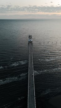 A stunning aerial shot of a long pier stretching into the ocean in Brisbane, showcasing a peaceful summer landscape.