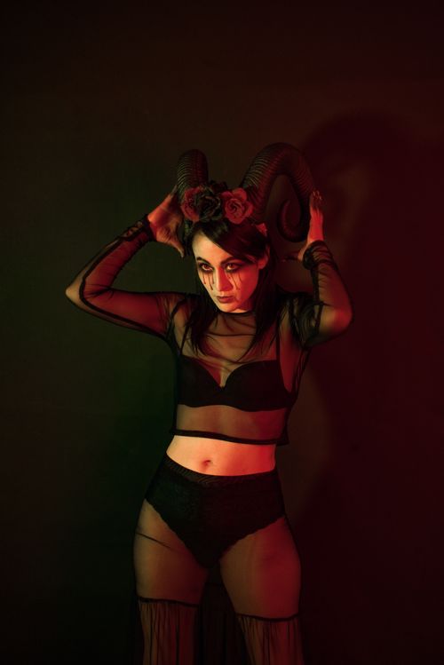 Free Woman in gothic costume with ram horns and dramatic makeup in moody lighting. Stock Photo
