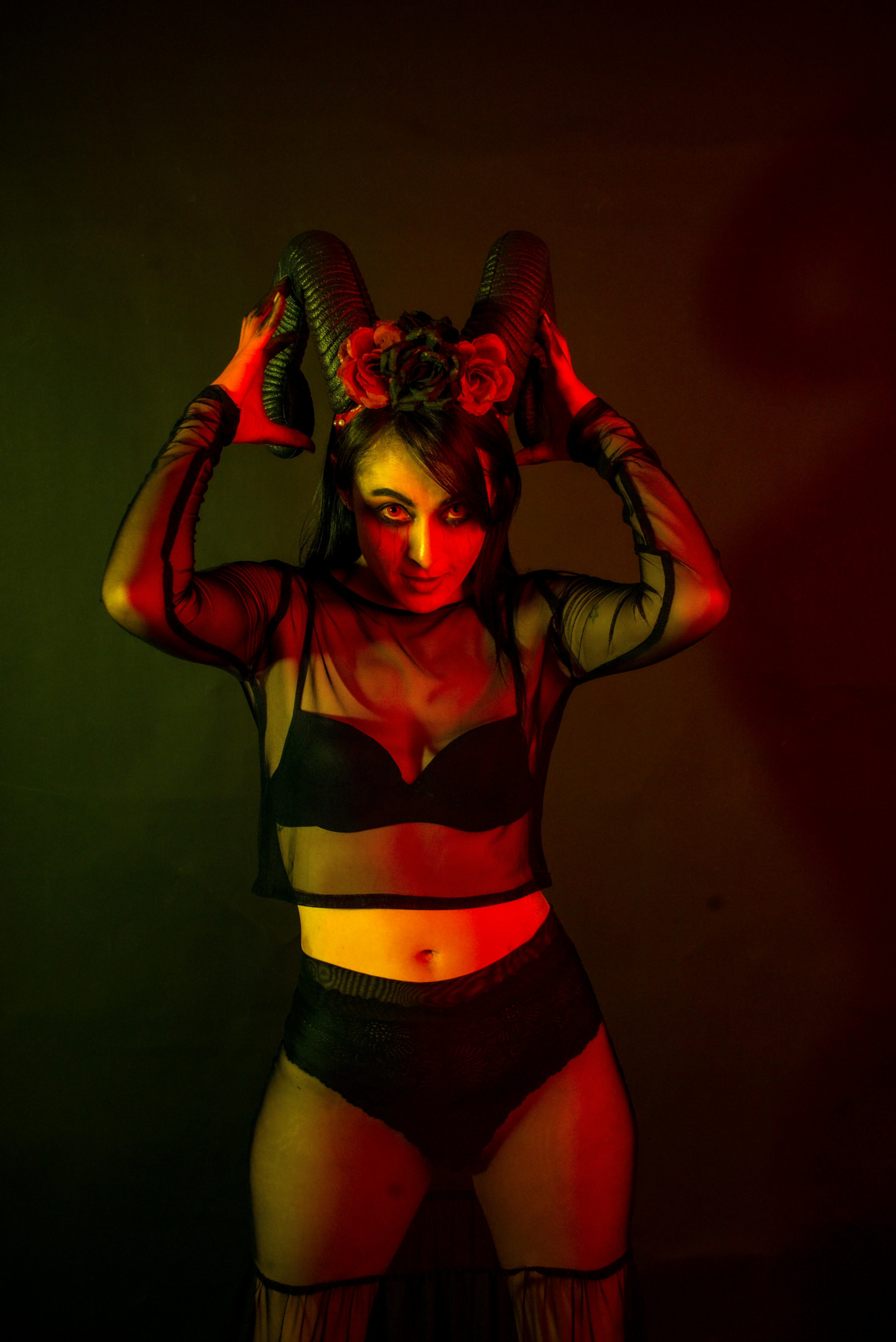 grátis Uma mulher com uma roupa escura e chifres posa ameaçadoramente sob uma iluminação dramática, evocando temas de mistério e fantasia. Foto profissional