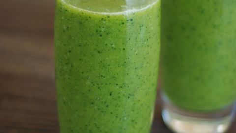Two green smoothies in glass on a rustic wooden table, embodying freshness and health.