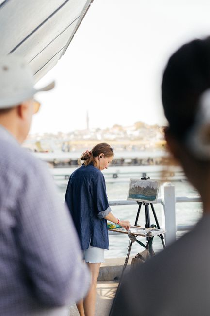 Artist painting en plein air in a picturesque urban riverside scene with onlookers.